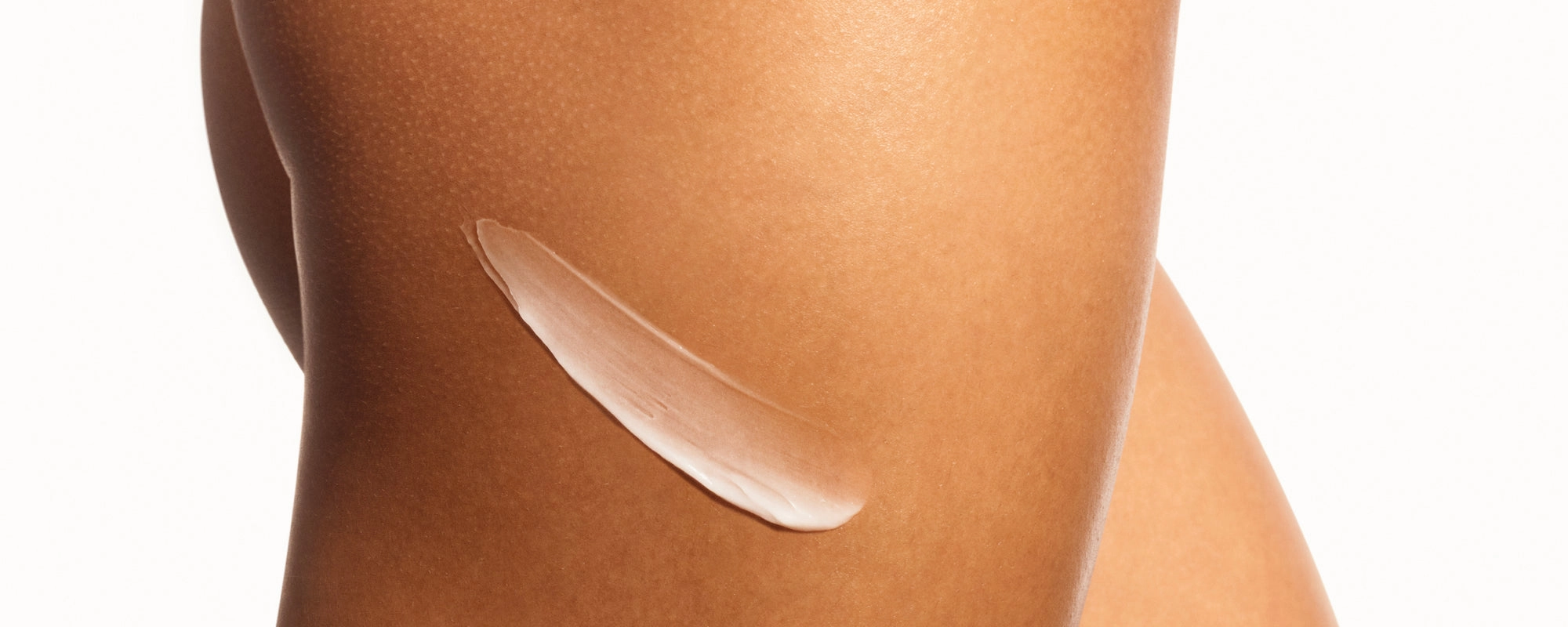 A single swipe of white cream across tanned skin against a pale background